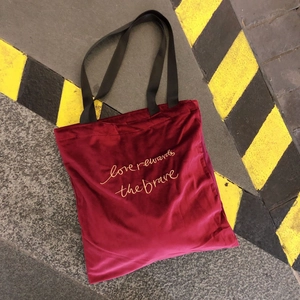 Close-up of golden letter embroidery on burgundy velvet tote bag texture and design