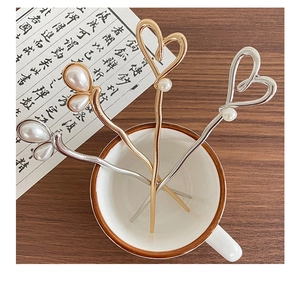 Detail of four metallic hairpins with faux pearls in a white cup on wood table