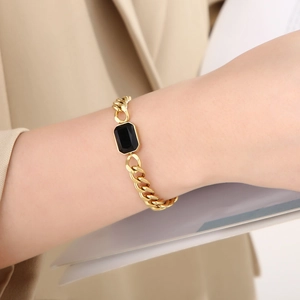 Gros plan sur un bracelet gourmette doré avec une pierre de cristal noir facettée
