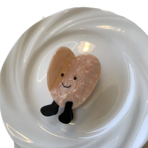 Pinza per capelli a cuore in acetato rosa con smiley su un piatto di ceramica bianco