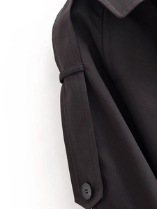 Detail of black double-breasted trench coat showing twill fabric texture and dark button