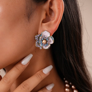 Gros plan de boucles d'oreilles fleurs en émail avec cristaux et perle sur modèle
