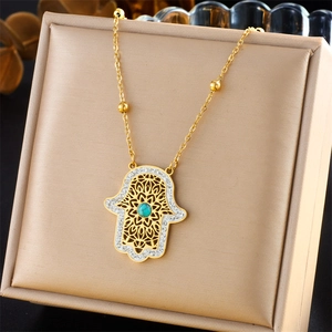 Goldene Hamsa-Halskette mit Türkisstein und weißen Diamanten in einer beigen Schmuckschatulle