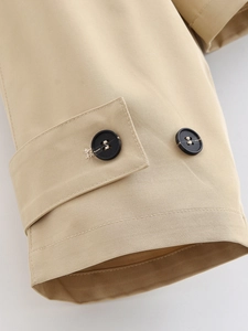 Detailed close-up of khaki trench coat cuff with two black buttons and twill fabric texture