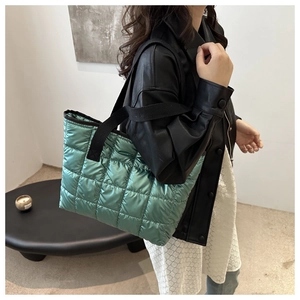 Detail view of glossy green quilted puffer bag featuring black woven handles