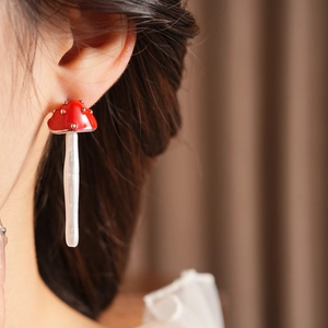 Macro close-up of a model wearing red mushroom stud earrings with white spotted details