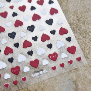 Macro detail of tricolor heart nail stickers featuring love text and embossed patterns