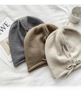 Close-up of rib-knit beanies with bow details in grey, tan, and beige colors