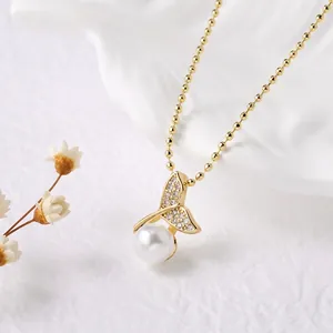 Dettaglio di una collana a coda di pesce dorata con perle e strass su un piatto decorativo