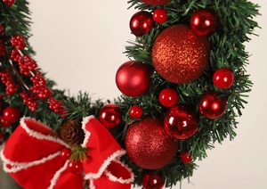 Close-up of red Christmas wreath with velvet bows, pine cones, and shiny berry ornaments