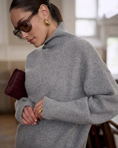 Detail of a grey oversized turtleneck knit sweater paired with a red woven clutch bag