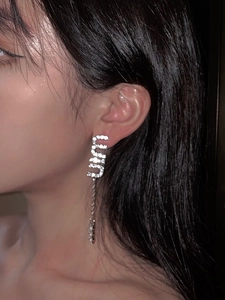 Detail of silver long tassel earrings with sparkling rhinestones in letter M shape