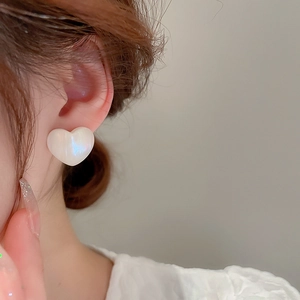 Close-up of elegant acrylic heart earrings with iridescent luster on a model's ear