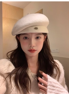 Detail shot of a cream wool beret featuring a vintage metal ML letter emblem for women