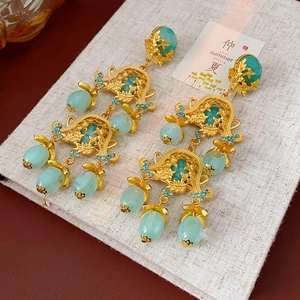 Detail view of vintage court-style earrings with hollow gold floral patterns and green gems