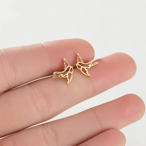 Macro shot of minimalist hollow bird stud earrings in gold on finger for size reference