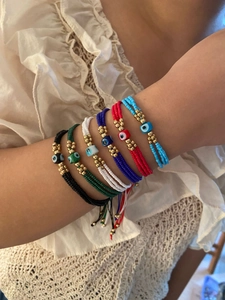 Detail of colorful woven evil eye bead bracelets set with adjustable gold accents