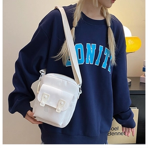 Close-up of a white canvas crossbody bag with front pocket flap worn by a model