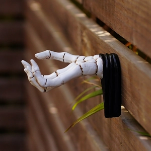 Macro detail of a white 3D skeleton hand wall hook mounted on a wooden garden fence