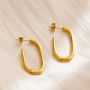 Detailed view of polished gold U-shape earrings on soft silk fabric background