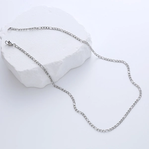 Macro shot of silver stainless steel Figaro chain necklace resting on a white textured stone