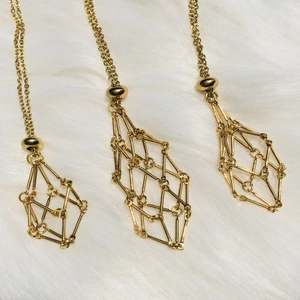 Three golden geometric mesh cage pendant necklaces displayed on soft white fur background