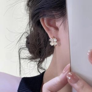 Close-up of golden white flower earrings with small central stone on a model's earlobe