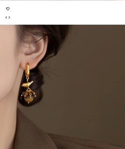 Detail of 18k gold bird earrings with tiger eye stone and elegant tassel on model