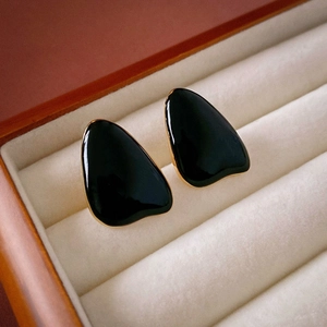 Close-up of black enamel teardrop earrings with gold plating in a beige velvet jewelry box