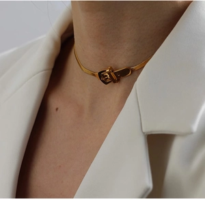 Detailed view of a gold belt buckle pendant on a minimalist choker with white blazer
