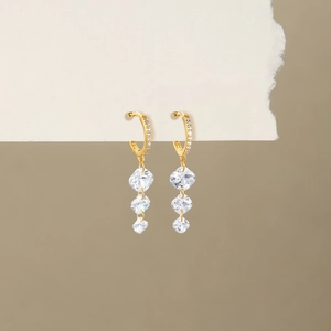 Detail of gold dangle earrings with sparkling square crystal tassels on beige card