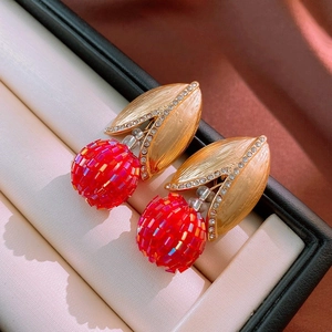 Détail de boucles d'oreilles dorées avec perles rouges et cristaux étincelants