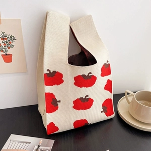 Beige knitted tote bag featuring a red persimmon pattern on a dark wooden table