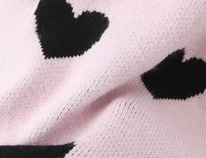 Macro shot of pink knitted fabric detail featuring a black heart-shaped jacquard pattern