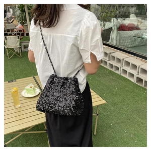 Outdoor model shot of a black sequined drawstring bucket bag with a chain strap