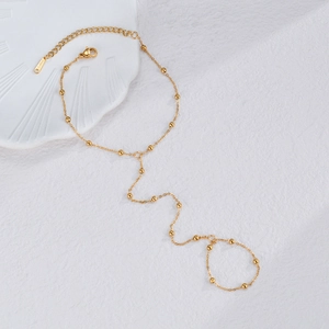 Golden stainless steel slave bracelet with small beads shown on a textured surface