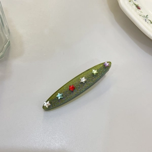 Detail of a green glitter hair clip with colorful resin star studs in a close-up shot