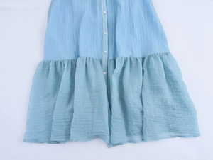 Macro view of light blue sleeveless maxi dress showing buttons and pleated fabric texture