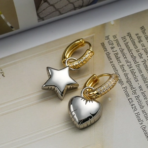 Asymmetric gold and silver drop earrings with heart and star charms on an open book