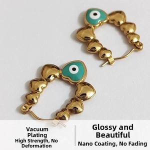 Detail of gold heart earrings with green enamel evil eye charm and vacuum plating