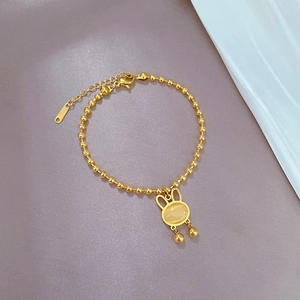 Macro detail of gold beaded bracelet featuring a rabbit charm with cat eye stone inlay
