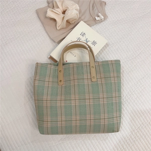 Macro shot of green plaid canvas tote bag with leather straps and metal rivets detail