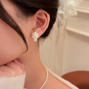 Close-up view of elegant flower basket pearl stud earrings worn by a model in warm light