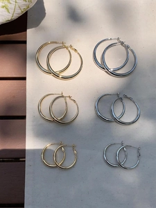 Polished gold and silver hoop earrings in three sizes displayed on a rustic background