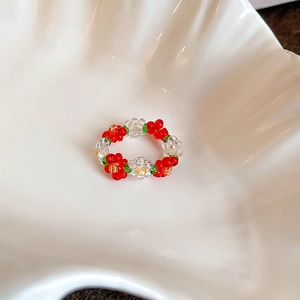 Close-up of handmade glass bead flower ring with red and white petals on a ceramic dish