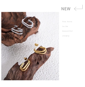 Detail of minimalist gold and silver U-shaped double hoop earrings on dark wood