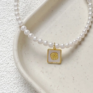 Gold plated copper necklace with square mother of pearl rose pendant on a ceramic tray