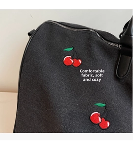 Detail of black canvas tote bag featuring red cherry embroidery and leather handles