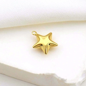 Polished gold star pendant with hanging ring displayed on white textured stone background
