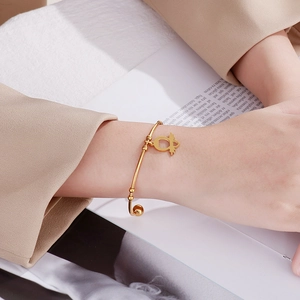 Detail of a gold-toned open cuff bracelet with an owl pendant on a model wrist